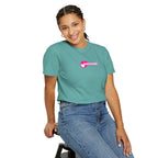 Person wearing a teal t-shirt with 'God is Good' text and pink heart design, sitting on a stool against a white background.
