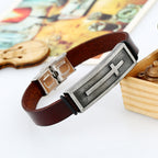 Brown leather bracelet with metal clasp and cross design on a light background