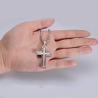 Hand holding a silver cross necklace against a plain background