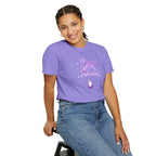 Person wearing a purple t-shirt with text and graphics, sitting on a stool against a white background