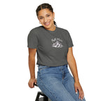 Person wearing a gray t-shirt with a mountain graphic and text, sitting on a stool against a white background