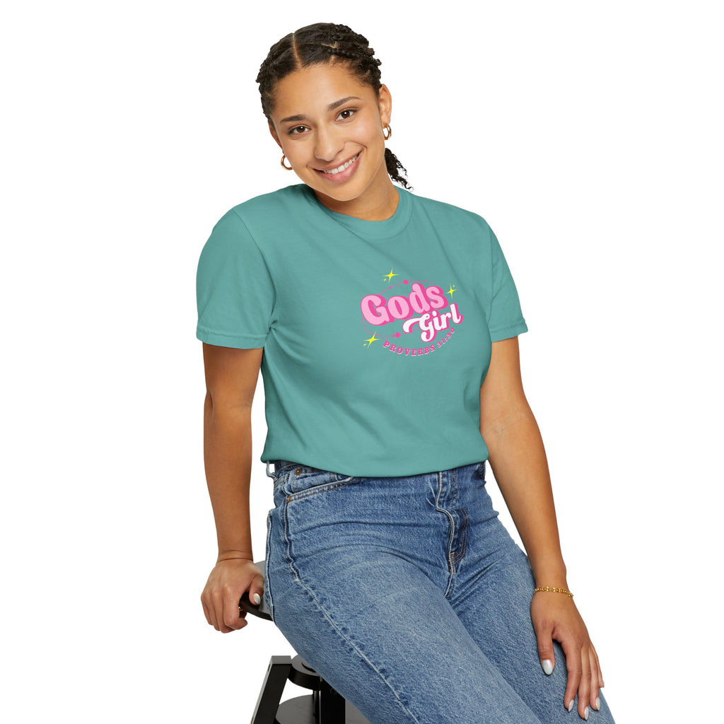 Person wearing a teal t-shirt with 'Gods girl' text, sitting on a stool against a white background