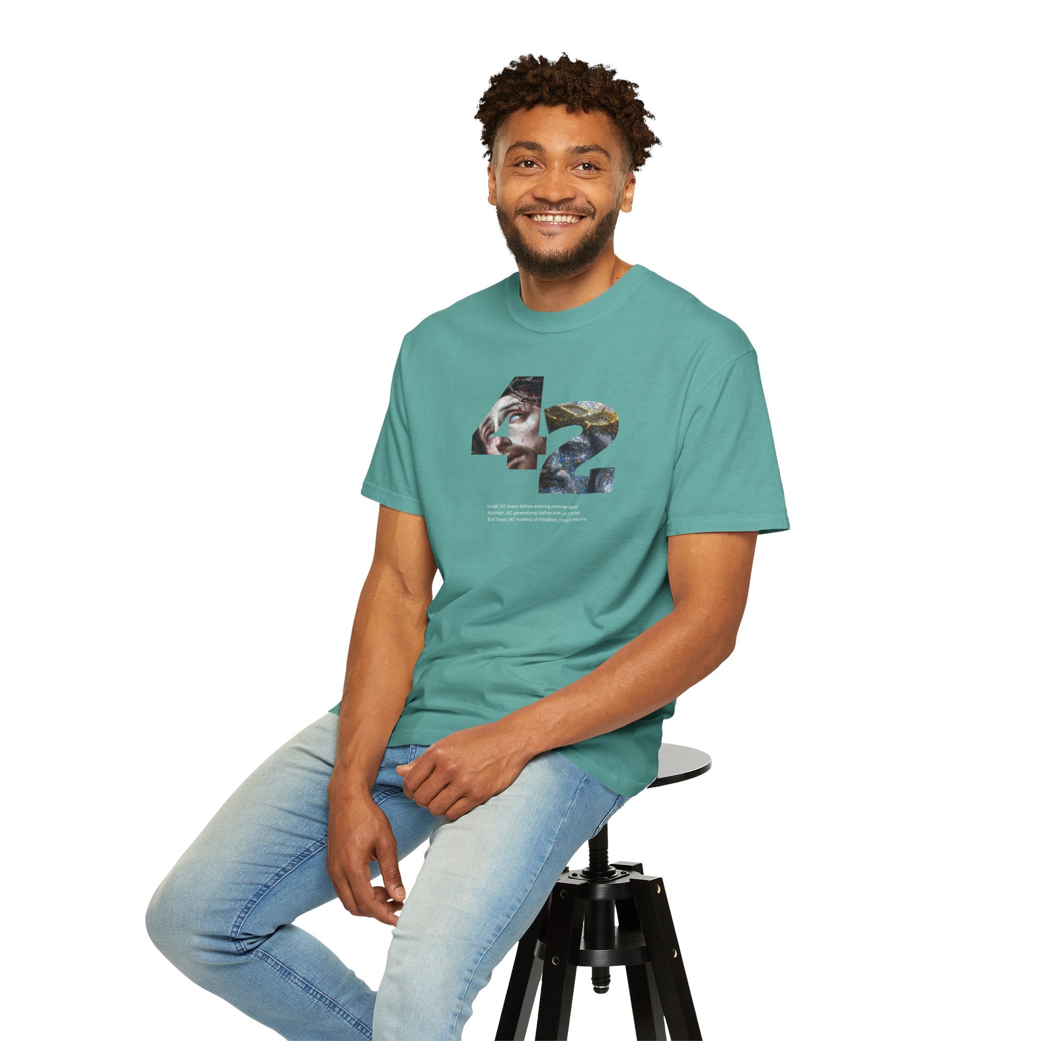 Man wearing a teal t-shirt with '2026 GRAD' text, sitting on a stool against a white background