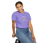 Person wearing a purple t-shirt with a mountain graphic and text, sitting on a stool against a white background