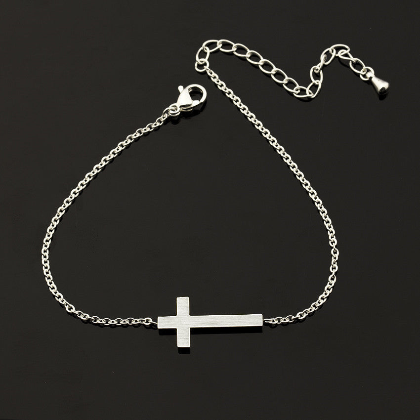 Silver chain bracelet with a cross pendant on a black background