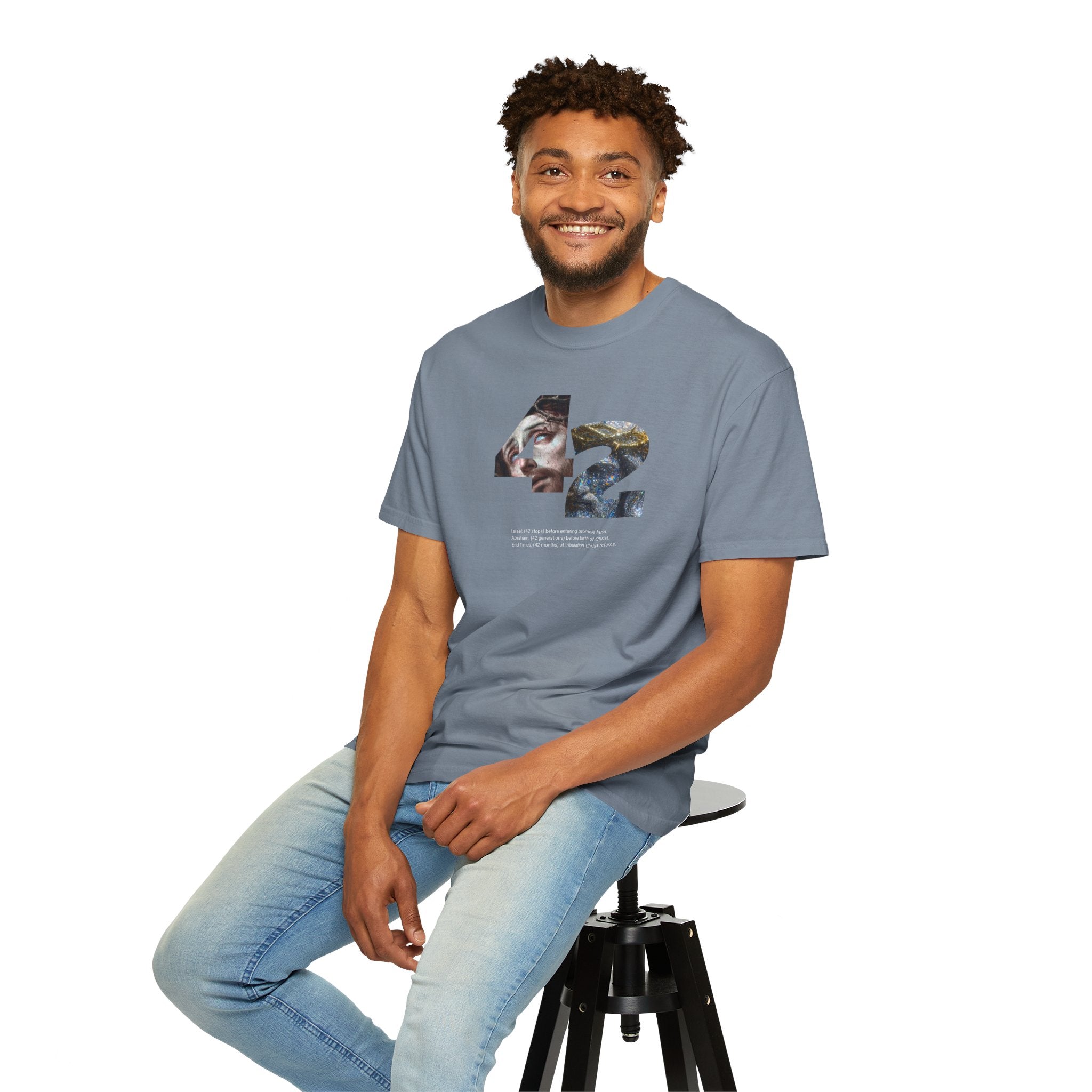 Man sitting on a stool wearing a gray t-shirt and light blue jeans against a white background