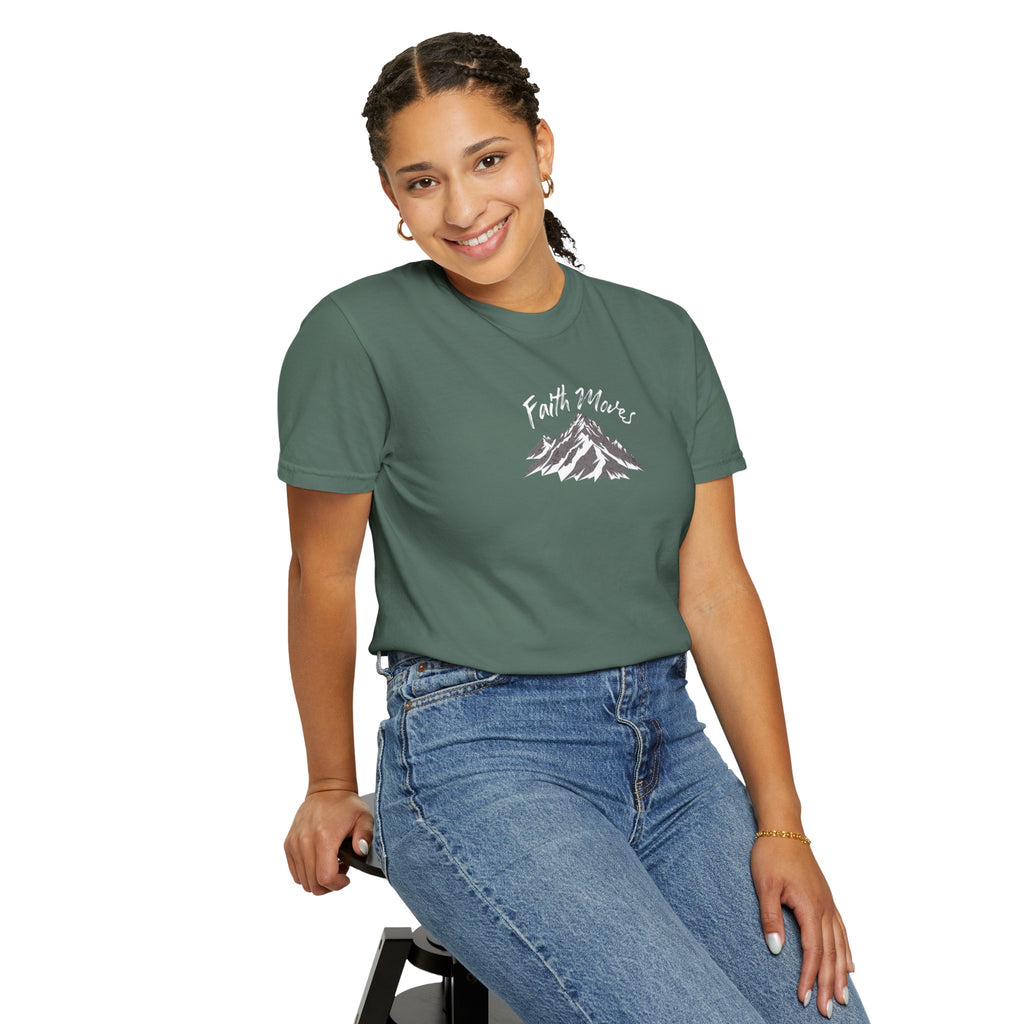 Person wearing a green t-shirt with a mountain graphic and text, sitting on a stool against a white background
