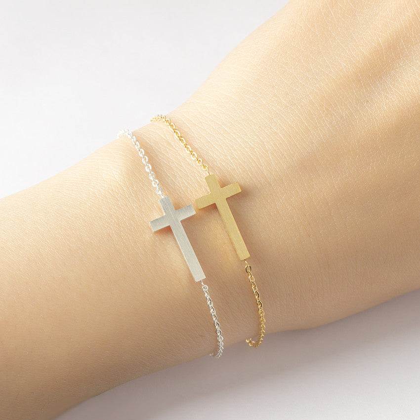 Two cross-shaped bracelets on a wrist against a light background