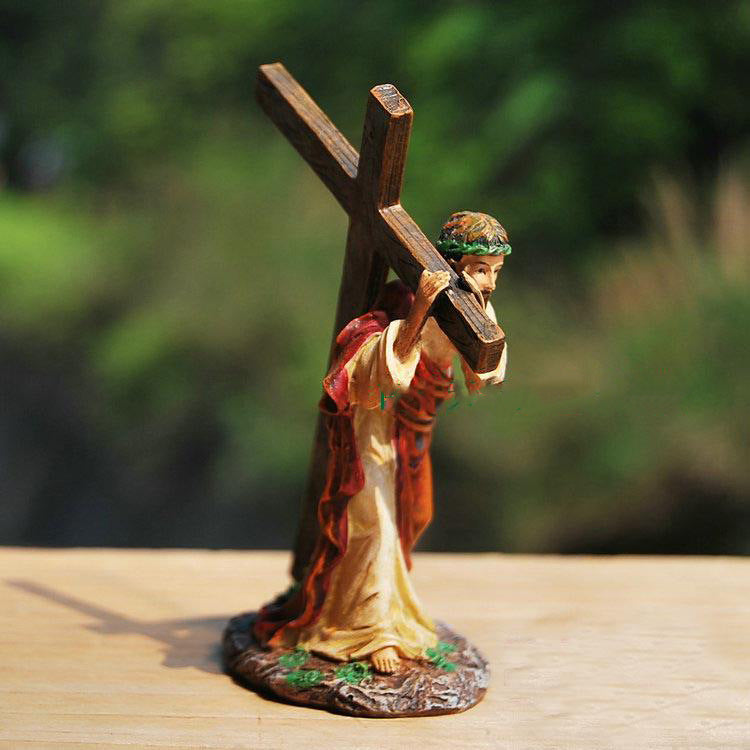 Statue of a person carrying a cross on a wooden surface with a blurred natural background