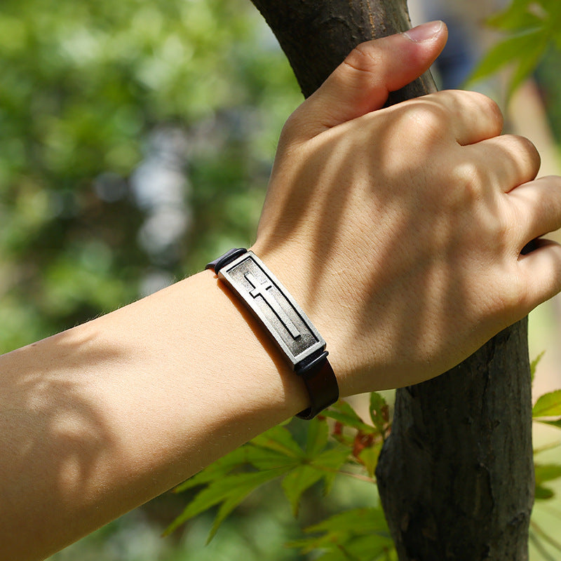 Hand wearing a black leather bracelet with metal clasp against a natural background