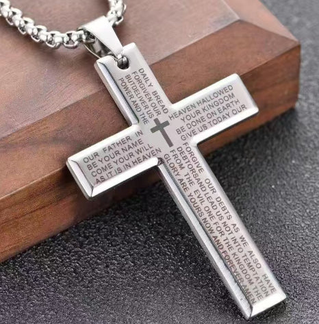 Silver cross pendant with engraved text on a wooden block