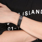 Person wearing a black bracelet on a black t-shirt with white text