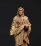 Wooden statue of a religious figure holding a heart symbol on a black background