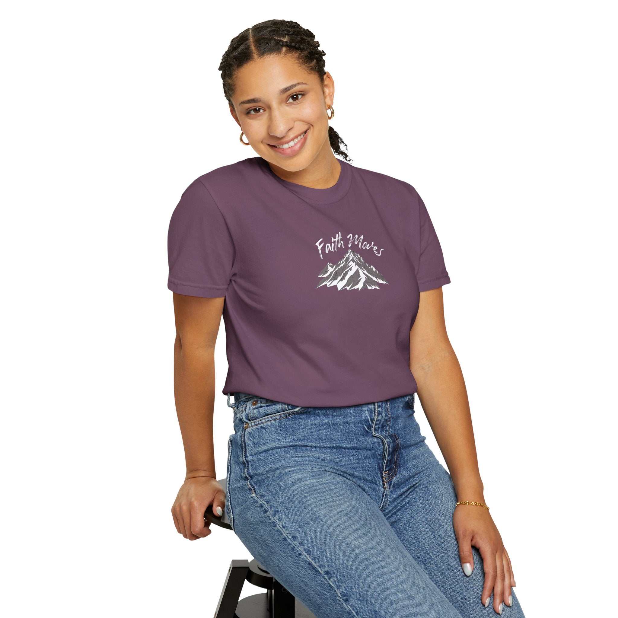 Person wearing a purple t-shirt with a mountain graphic and text, sitting on a stool against a white background