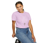Person wearing a purple t-shirt with text and a cross symbol, sitting on a stool against a white background