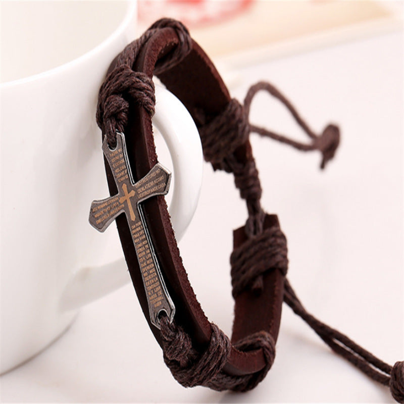 Brown braided leather bracelet with a silver cross charm on a white background