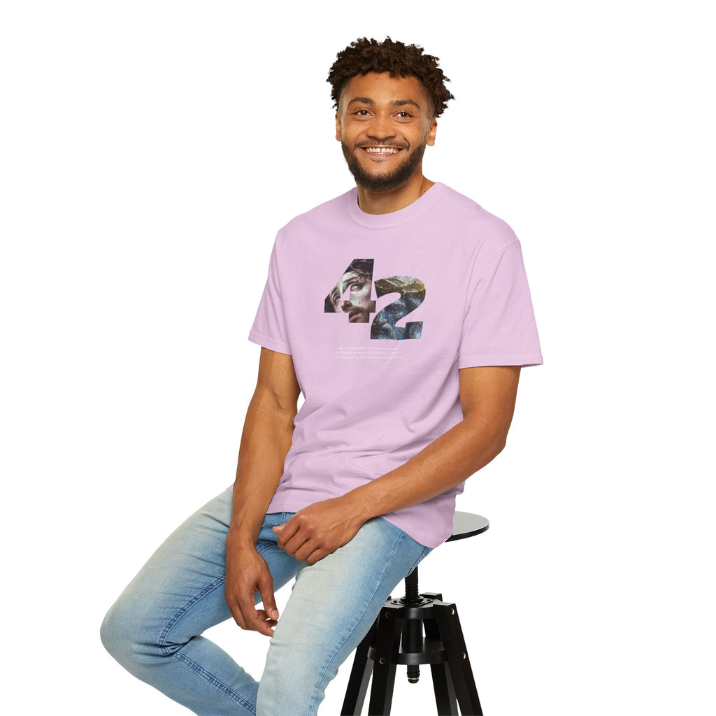 Man wearing a light purple t-shirt with a graphic design sitting on a stool against a white background
