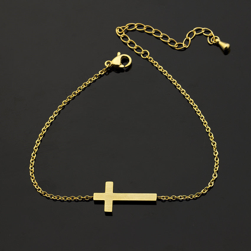 Gold bracelet with a cross pendant on a black background
