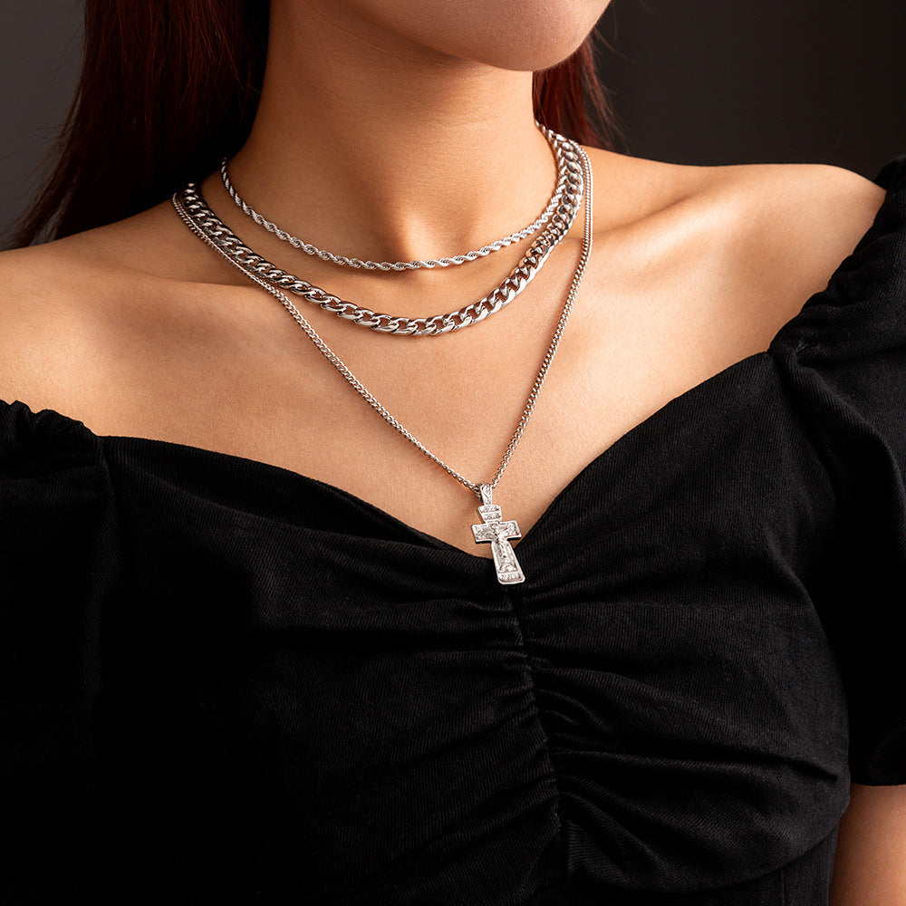 Person wearing a silver necklace with a cross pendant on a black background