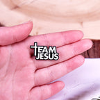 Hand holding a 'Team Jesus' badge with a cross symbol.