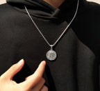 Silver necklace with a round pendant worn by a person in a black outfit.