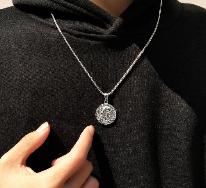 Silver necklace with a round pendant worn by a person in a black outfit.