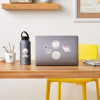 Laptop with stickers on a wooden desk with a water bottle and yellow chair.