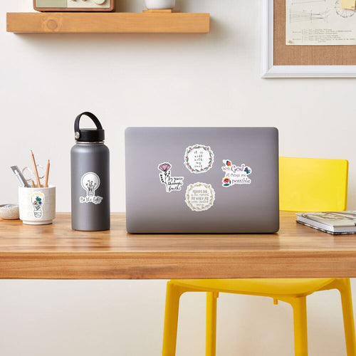 Laptop with stickers on a wooden desk with a water bottle and yellow chair.