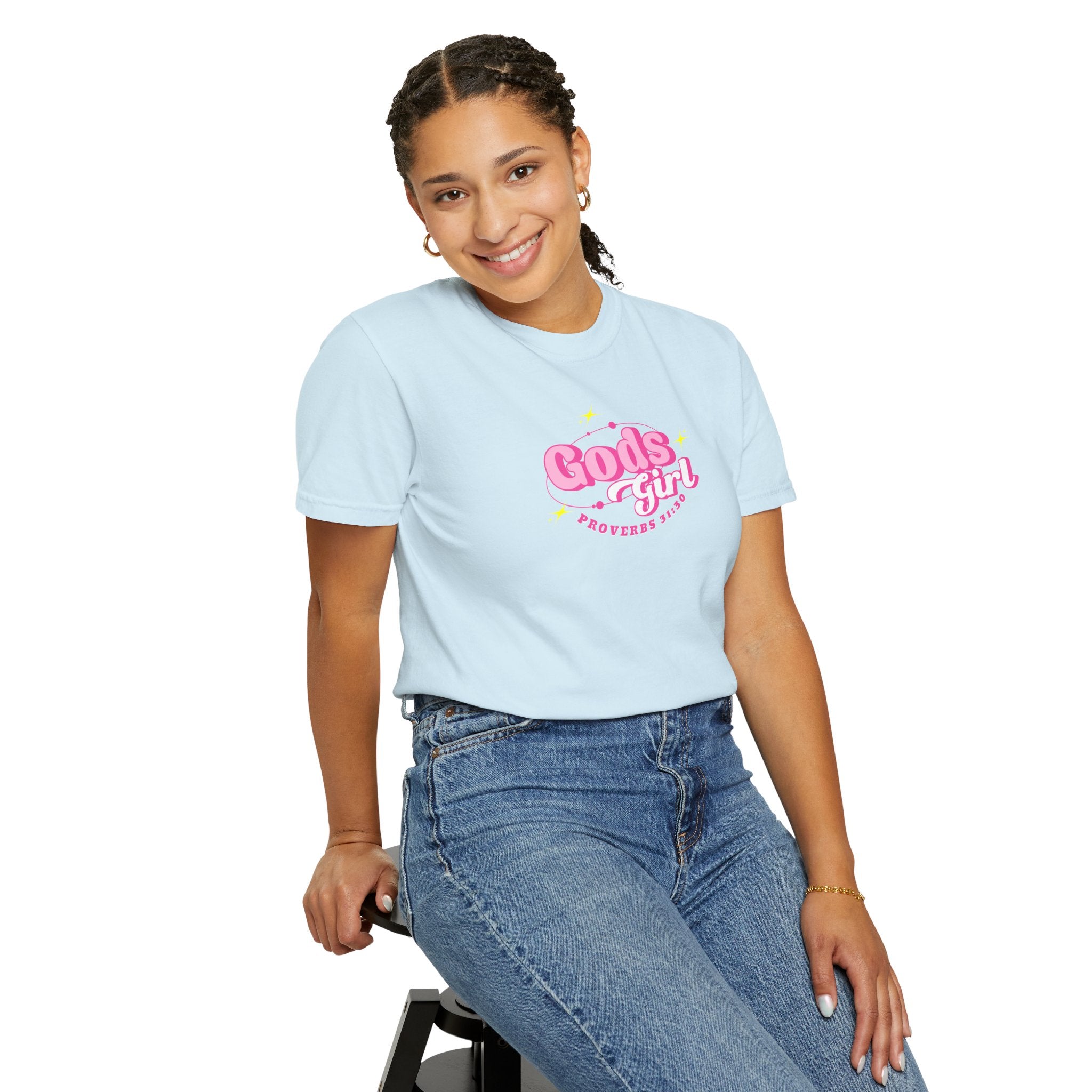 Person wearing a light blue t-shirt with 'God's girl' text, sitting on a stool against a white background