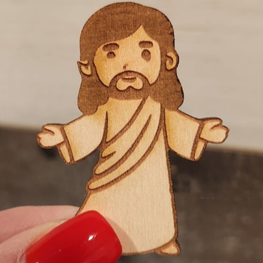 Wooden figurine of a religious figure with outstretched arms held by a person with red nail polish.