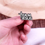 Hand holding a small object with 'Team Jesus' text overlay