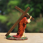Statue of a person carrying a cross on a wooden surface with a blurred green background