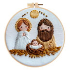 Embroidery hoop with a nativity scene design featuring an angel, a man, and a baby in a manger.